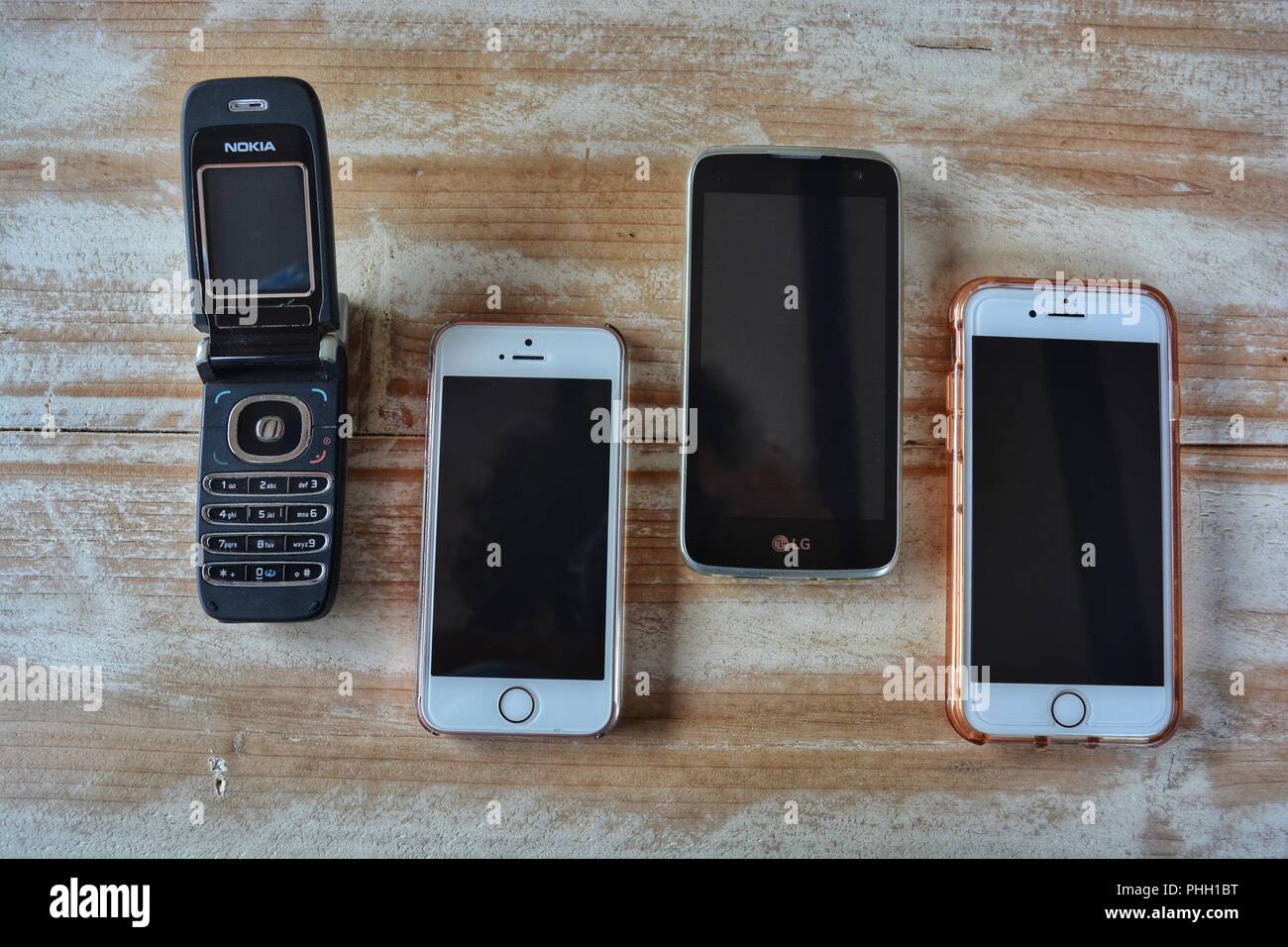 Nokia flip top phone, iPhone XE,  LG phone and  iPhone7 on a wooden tabletop with copy space Stock Photo