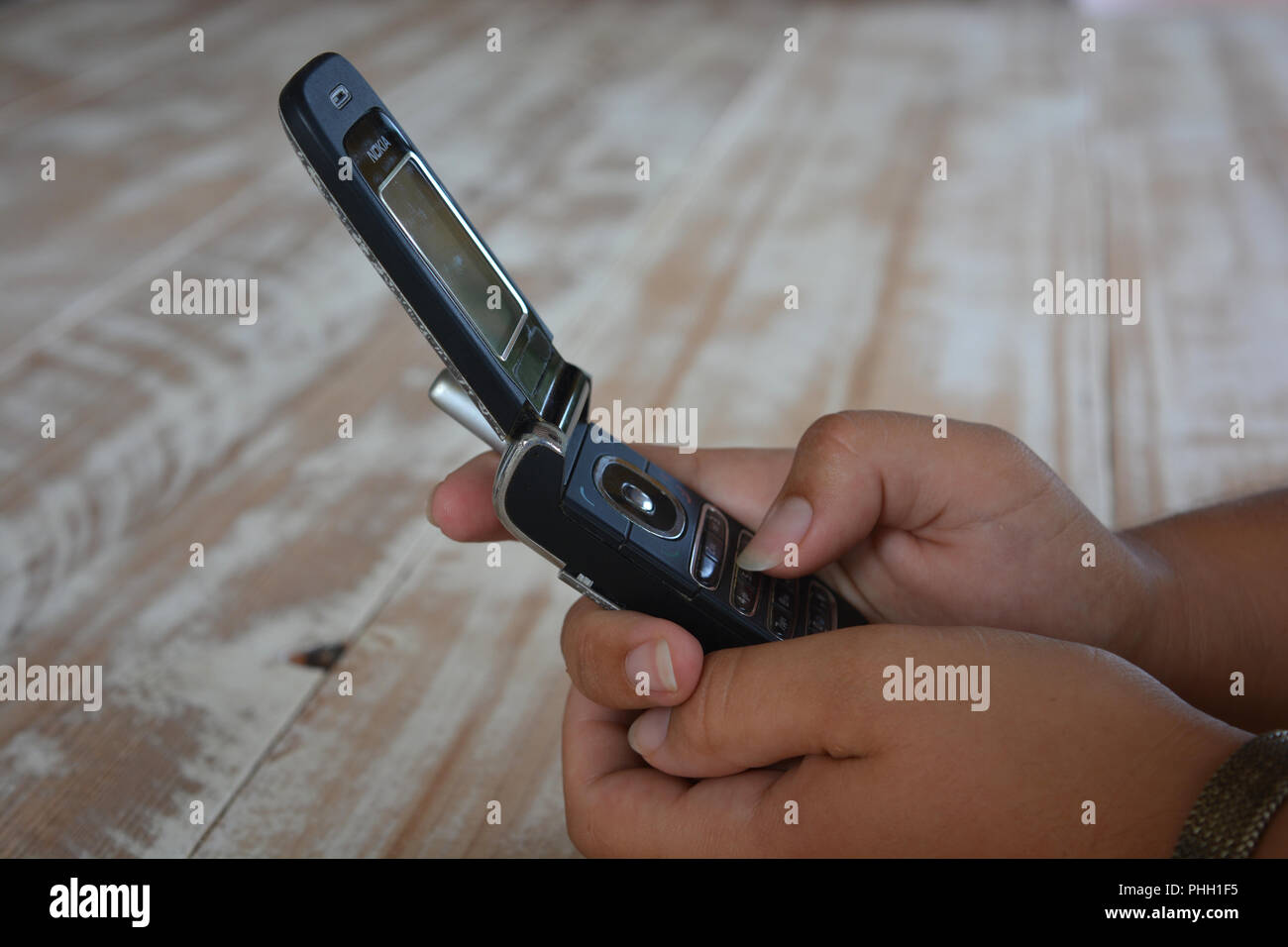 An old fashioned Nokia flip phone in a woman's hands, against a wooden tabletop background with copy space Stock Photo