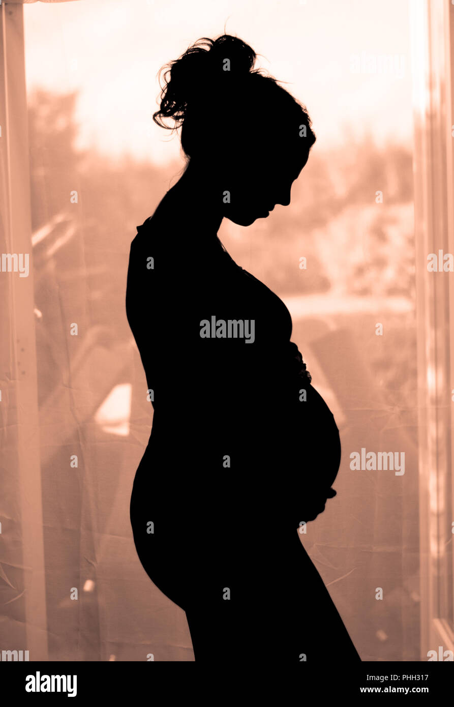 silhoutte of a pregnant lady cradling her baby bump Stock Photo