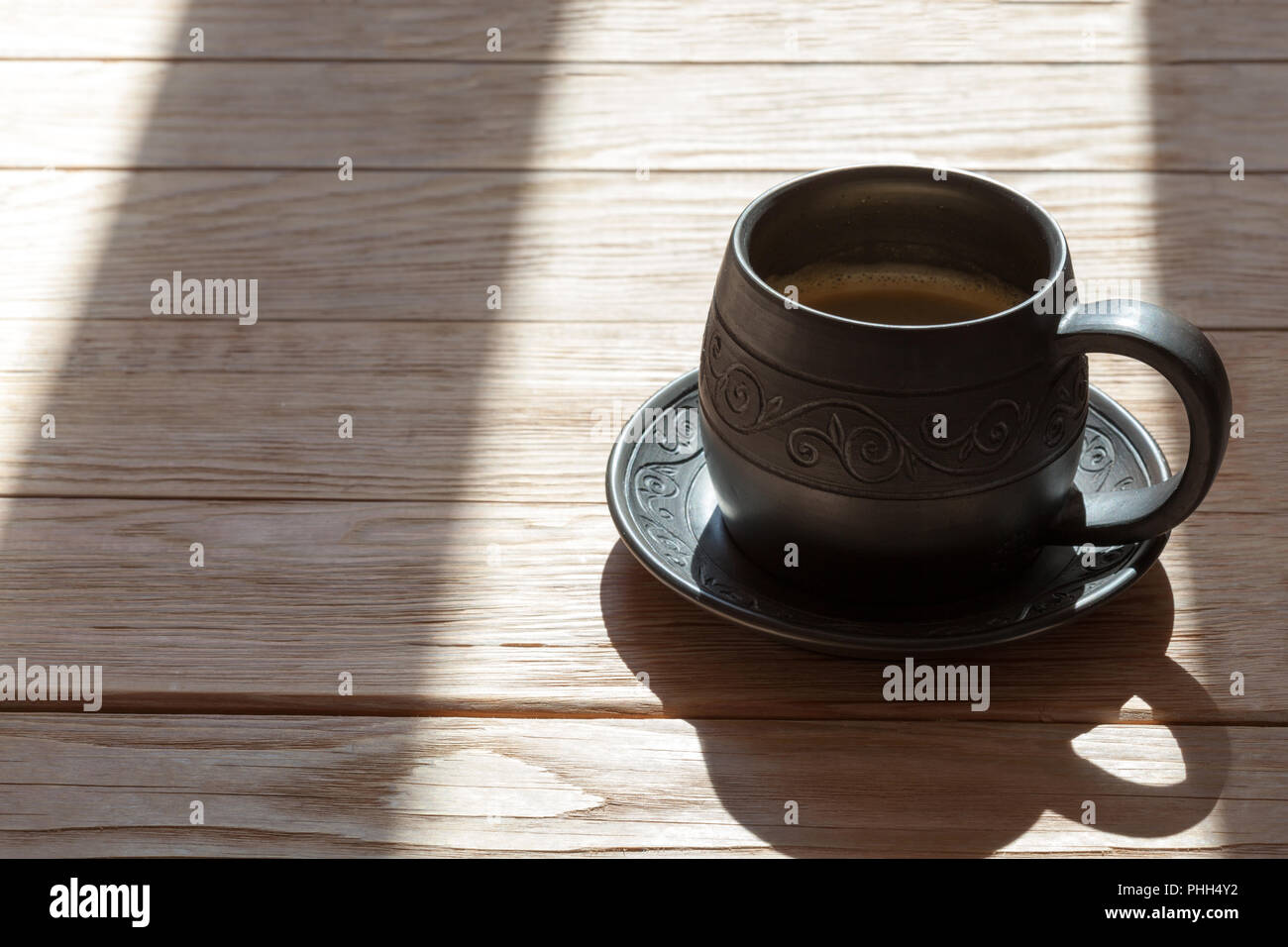 Ceramics handmade mug with coffee over wooden background with morning sunrays Stock Photo