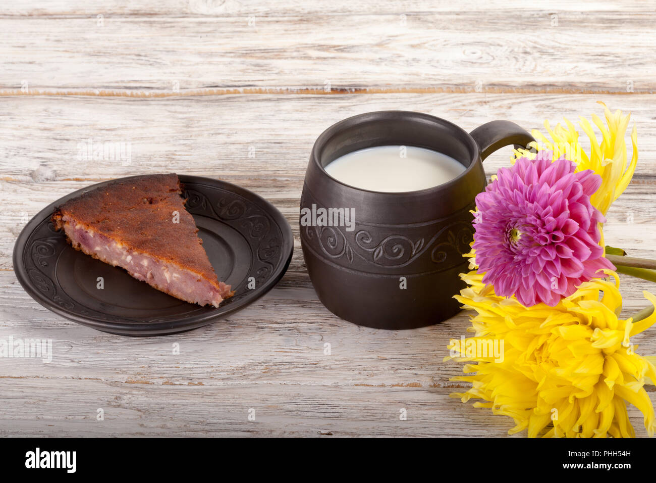 Ceramics handmade mug with milk, flowers and pie on wooden table Stock Photo