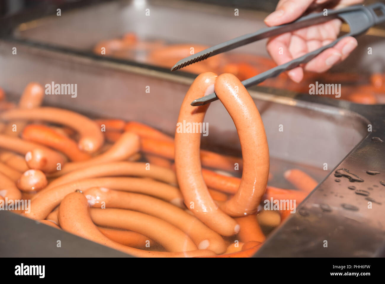Viennese sausages ready to be cooked are taken with forceps Stock Photo