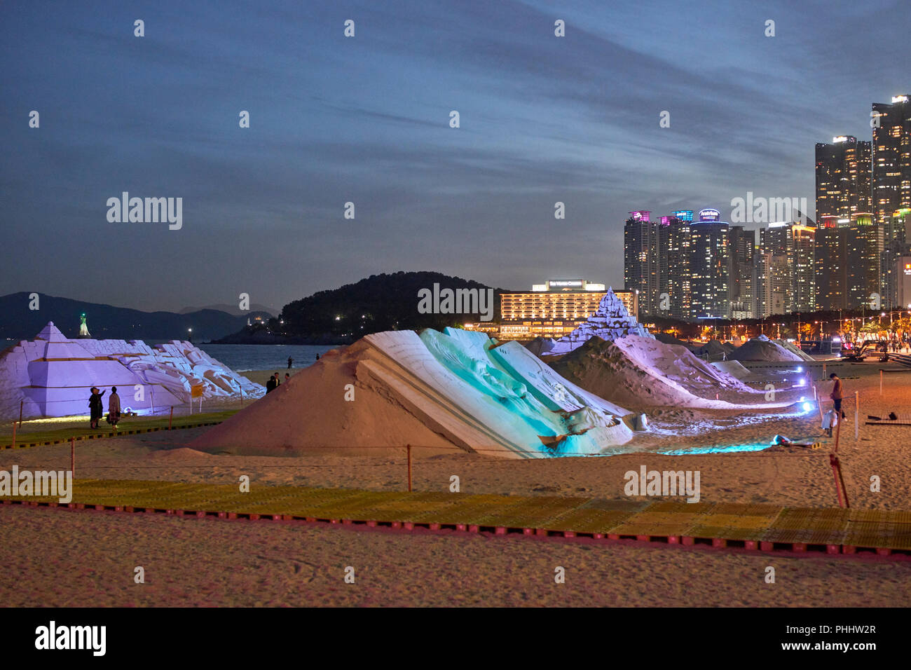 Haeundae Sand Festival 2018, Busan, Korea. Sculptures lit at twighlight with bay, Dongbaek Park and skyscrapers in background; lighthouse Stock Photo