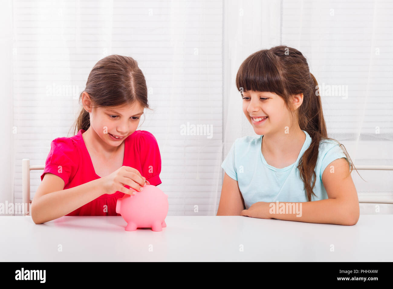 Cute little girls putting coin into piggy bank Stock Photo - Alamy
