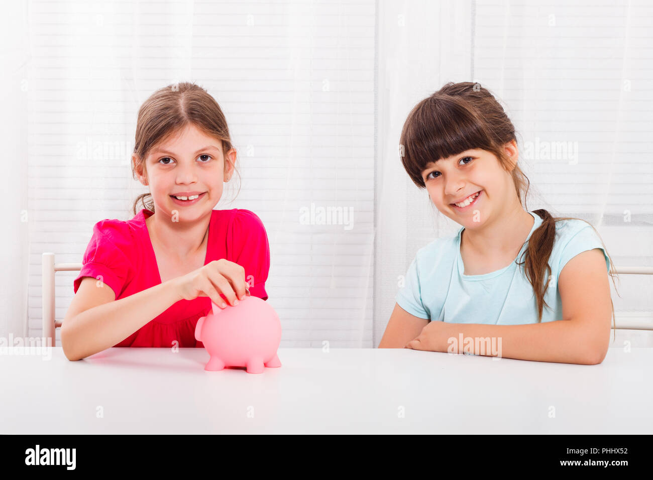 Cute little girls putting coin into piggy bank Stock Photo - Alamy