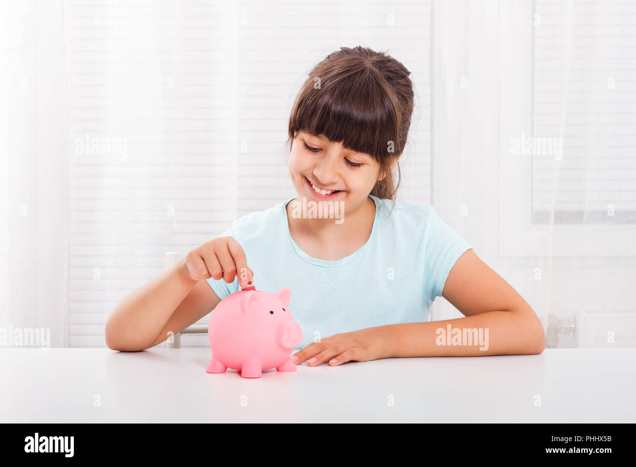 Cute little girl is putting coin into piggy bank Stock Photo - Alamy
