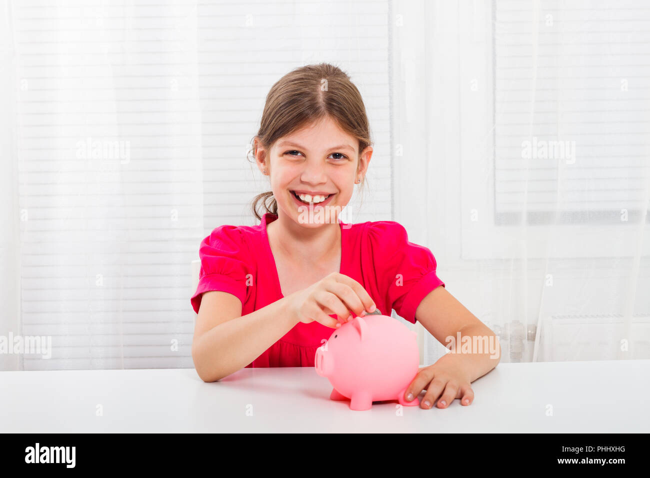 Cute little girl is putting coin into piggy bank Stock Photo - Alamy