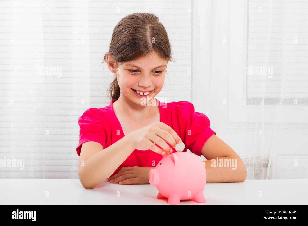 Cute little girl is putting coin into piggy bank Stock Photo - Alamy