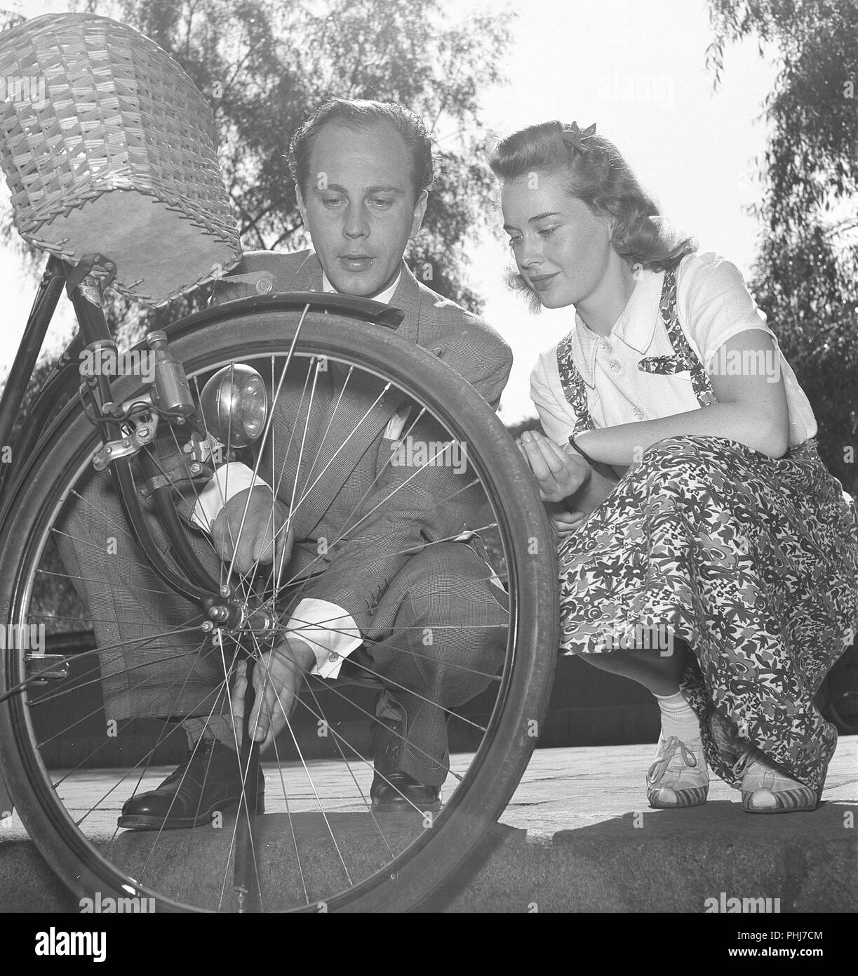 1940s couple with a bicycle. Actor Willy Peters is seen here pumping air into the tire of a womans bicycle while she is sitting beside him and looking. Sweden 1940s.  Photo Kristoffersson E50-3 Stock Photo