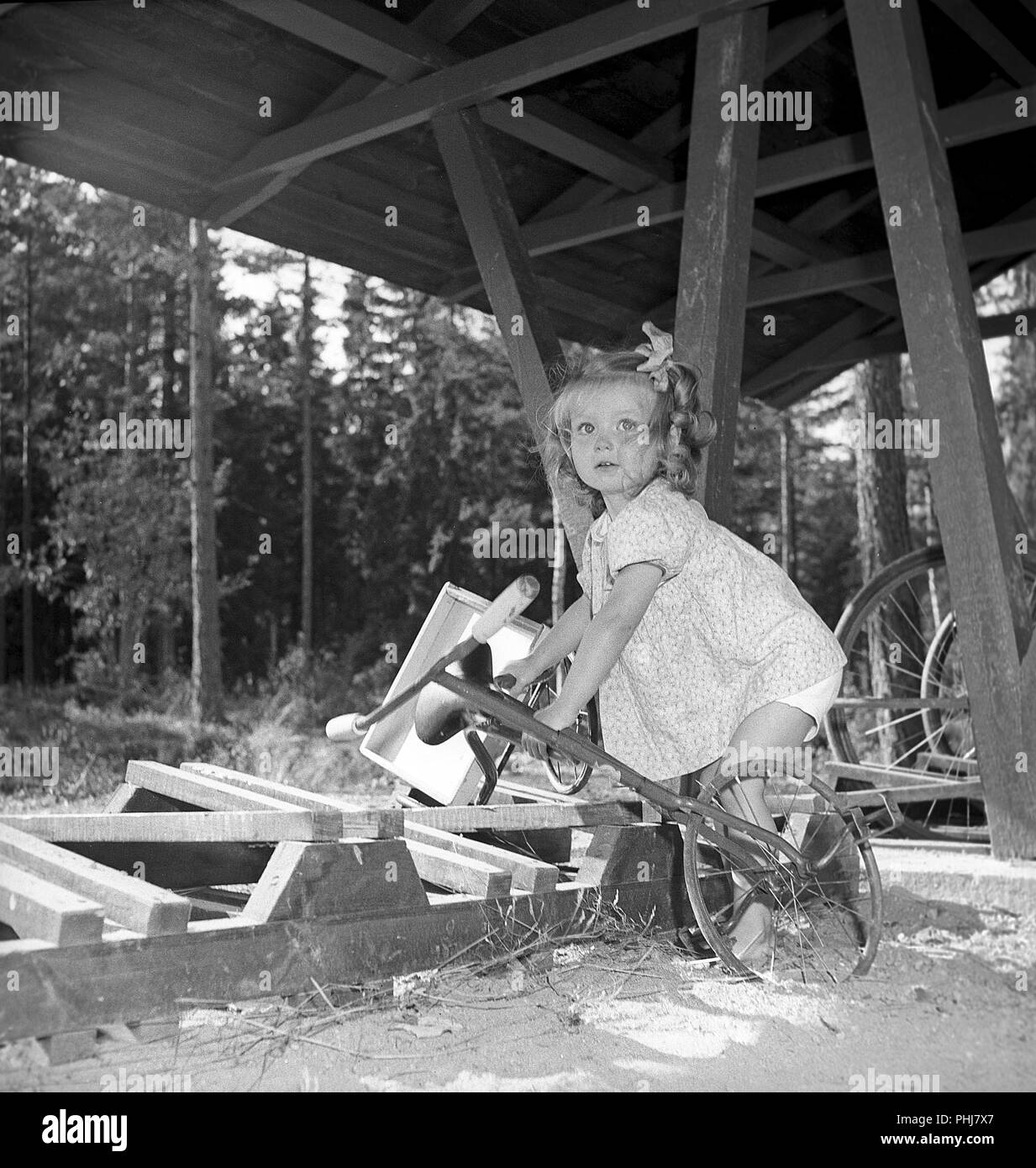 1940s girl. A little girl with her tricycle is having some difficulty when trying to get it out of the bicycle stand. Sweden 1947. Photo Kristoffersson V94-1 Stock Photo