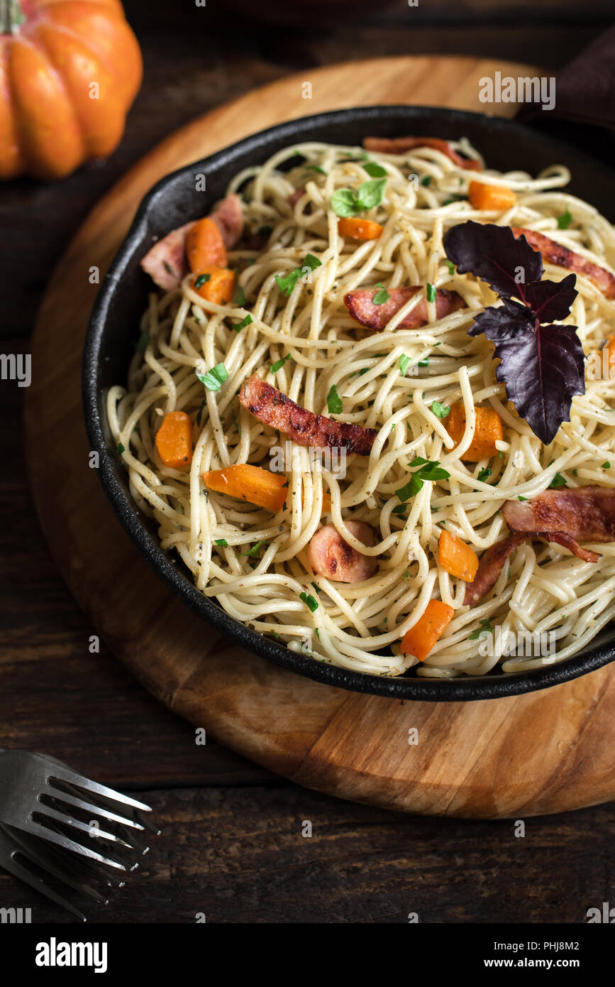 Autumn pasta with pumpkin and bacon in cast iron pan. Homemade spaghetti pumpkin pasta on wooden, copy space. Autumn food. Stock Photo
