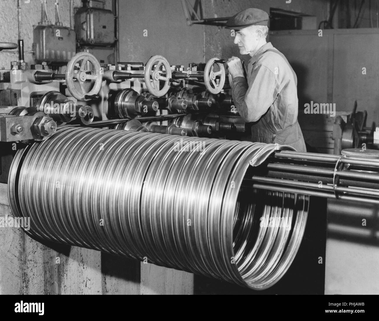 Factory in the 1950s. A worker at the bicycle and motorcycle company Monark in Sweden. The machine is producing steel rims to be used in the production of bicycles . Sweden 1958 Stock Photo