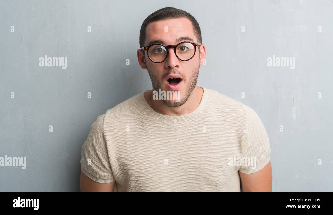 Young caucasian man over grey grunge wall scared in shock with a ...