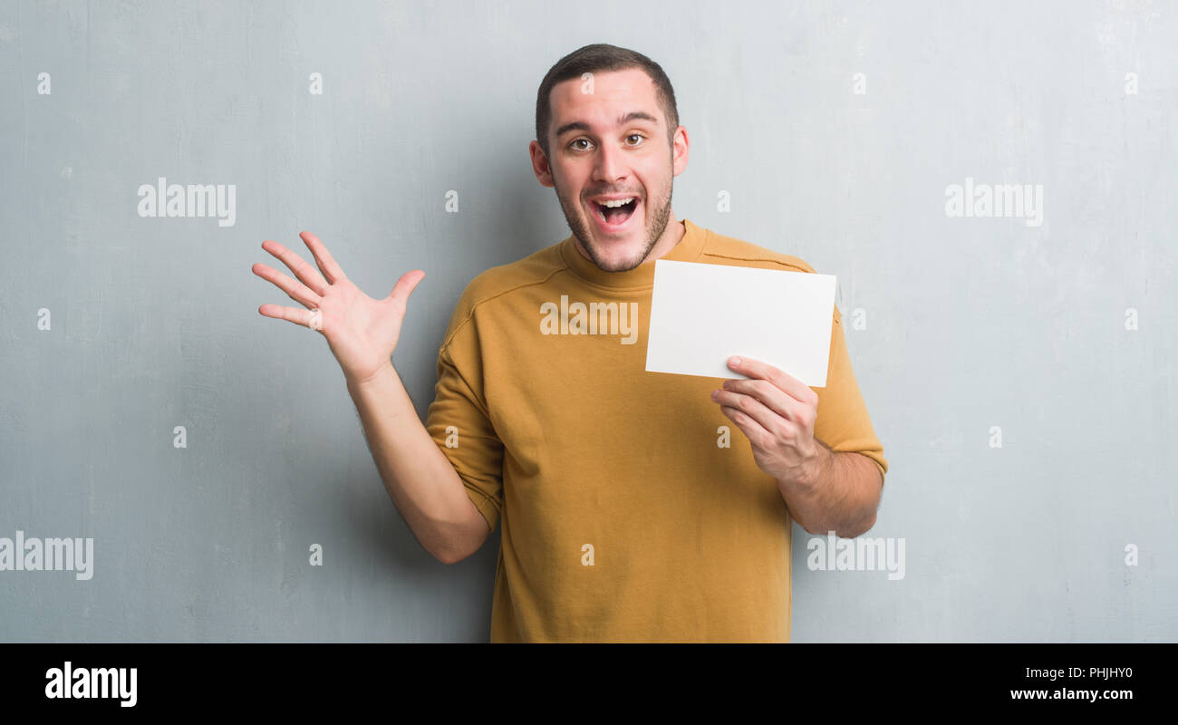 young caucasian man over grey grunge wall holding blank card