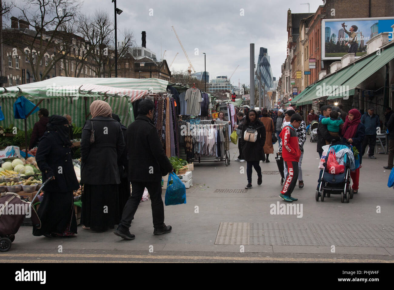 View of shoppers and market stalls on Whitechapel Road, Tower Hamlets, East London, looking towards the Gherkin (30 St Mary Axe) and the City, 2016. Stock Photo