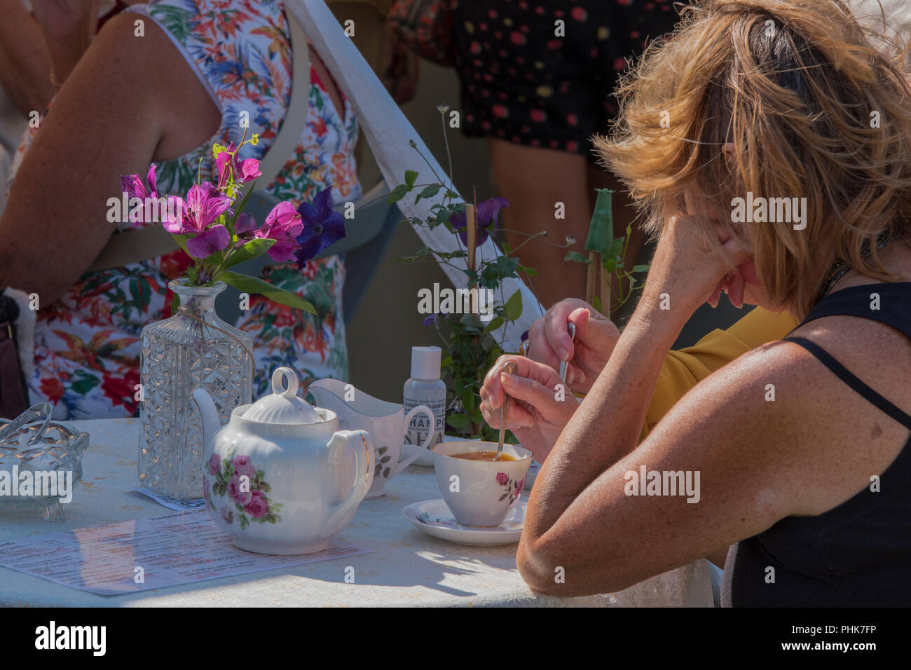 middle aged woman drinking tea from fine china teapot, cup and saucer