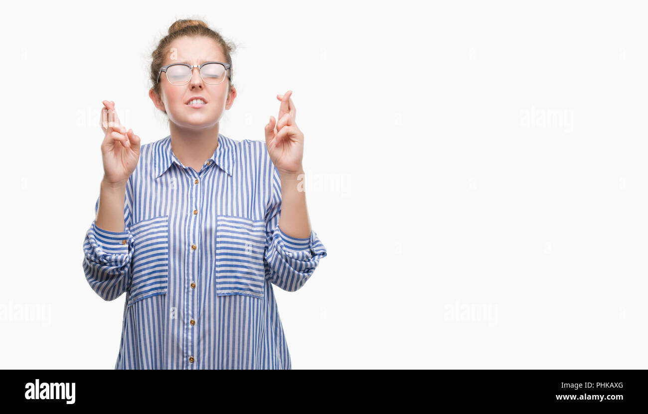 Young blonde business woman smiling crossing fingers with hope and eyes closed. Luck and superstitious concept. Stock Photo