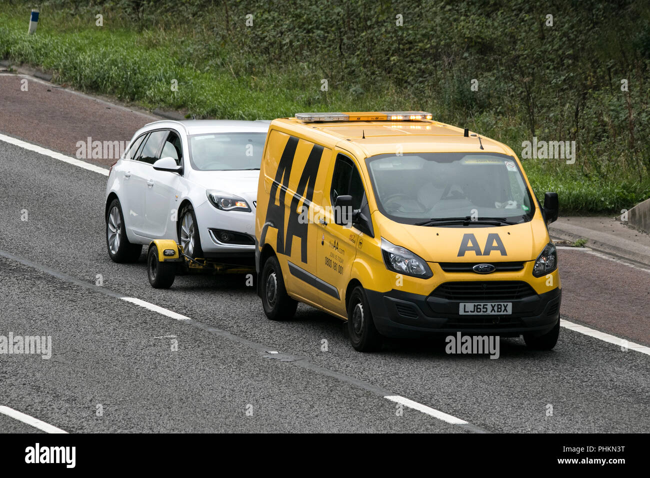 Yellow AA 24hr breakdown recovery vehicle towing trailer on the M6 motorway at Lancaster, UK Stock Photo