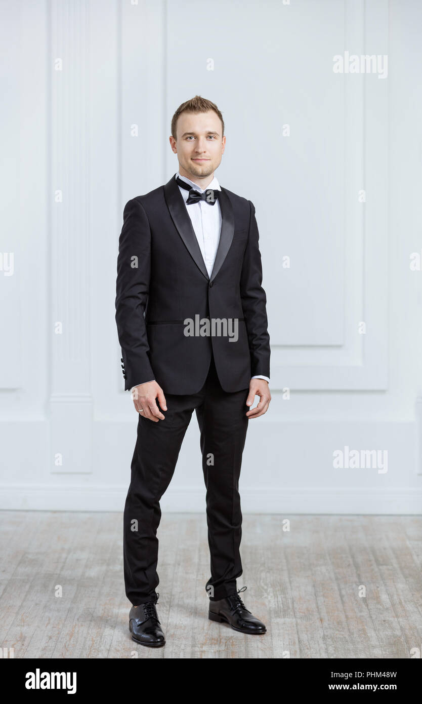 Attractive young man in tuxedo looking at camera indoors Stock Photo
