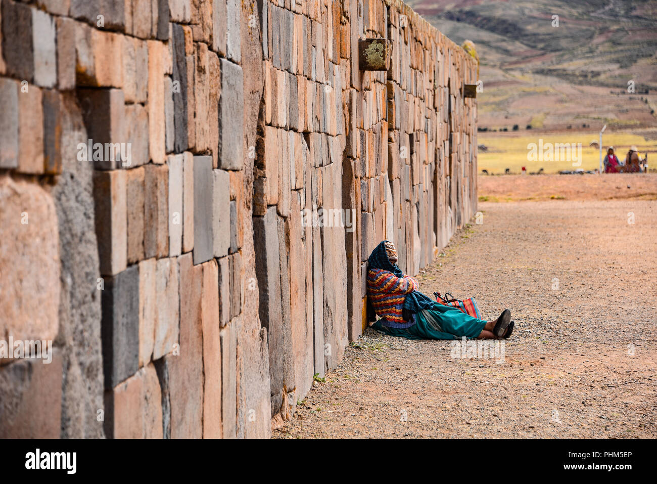 A local Andean lady rests against an intricately constructed stone wall at the Tiwanaku archaeological site, near La Paz, Bolivia Stock Photo