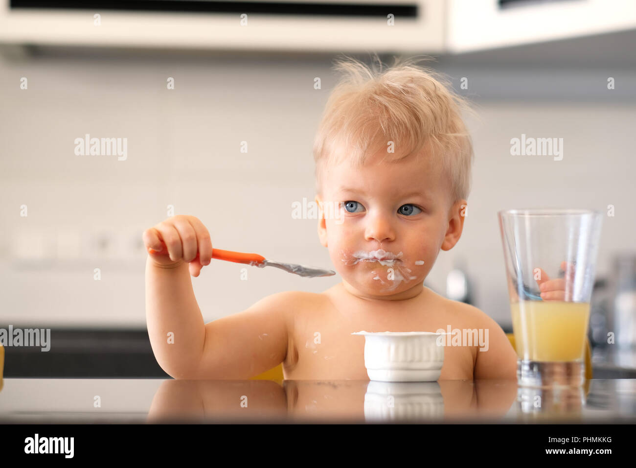 Adorable one year old baby boy eating yoghurt with spoon Stock Photo