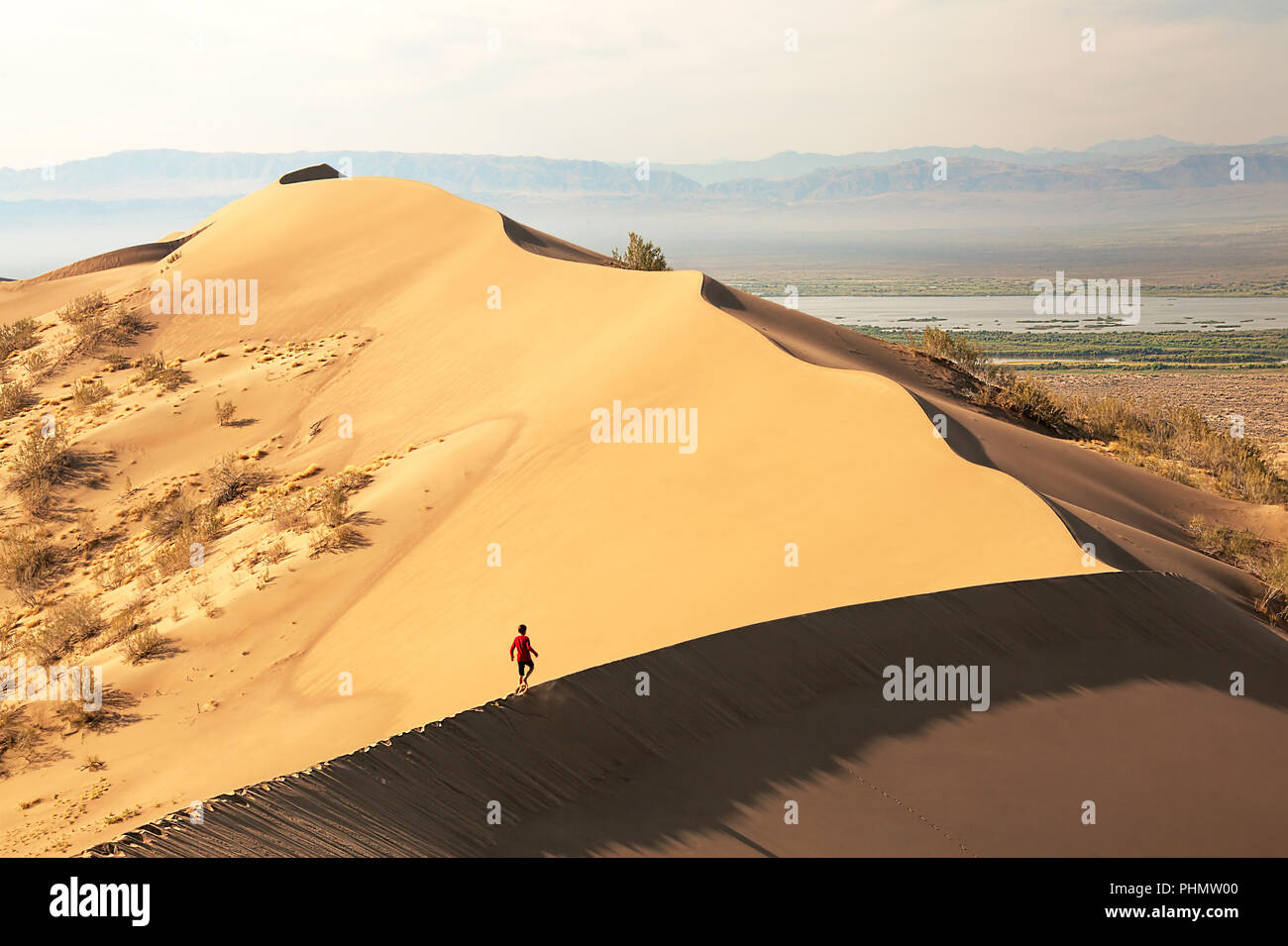 Concept: only the going one will master the way. Man walking on beautiful sand dunes at sunrise. Altyn-Emel semi-desert, Kazakhstan. Stock Photo
