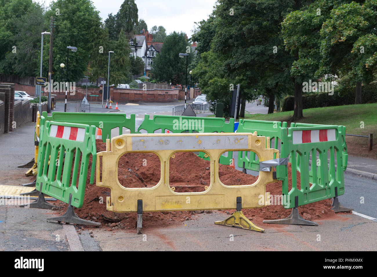 Roadworks in Kinver, Staffordshire, UK, with fenced off area around a hole in the road with yellow and green fence, road cones and signs Stock Photo