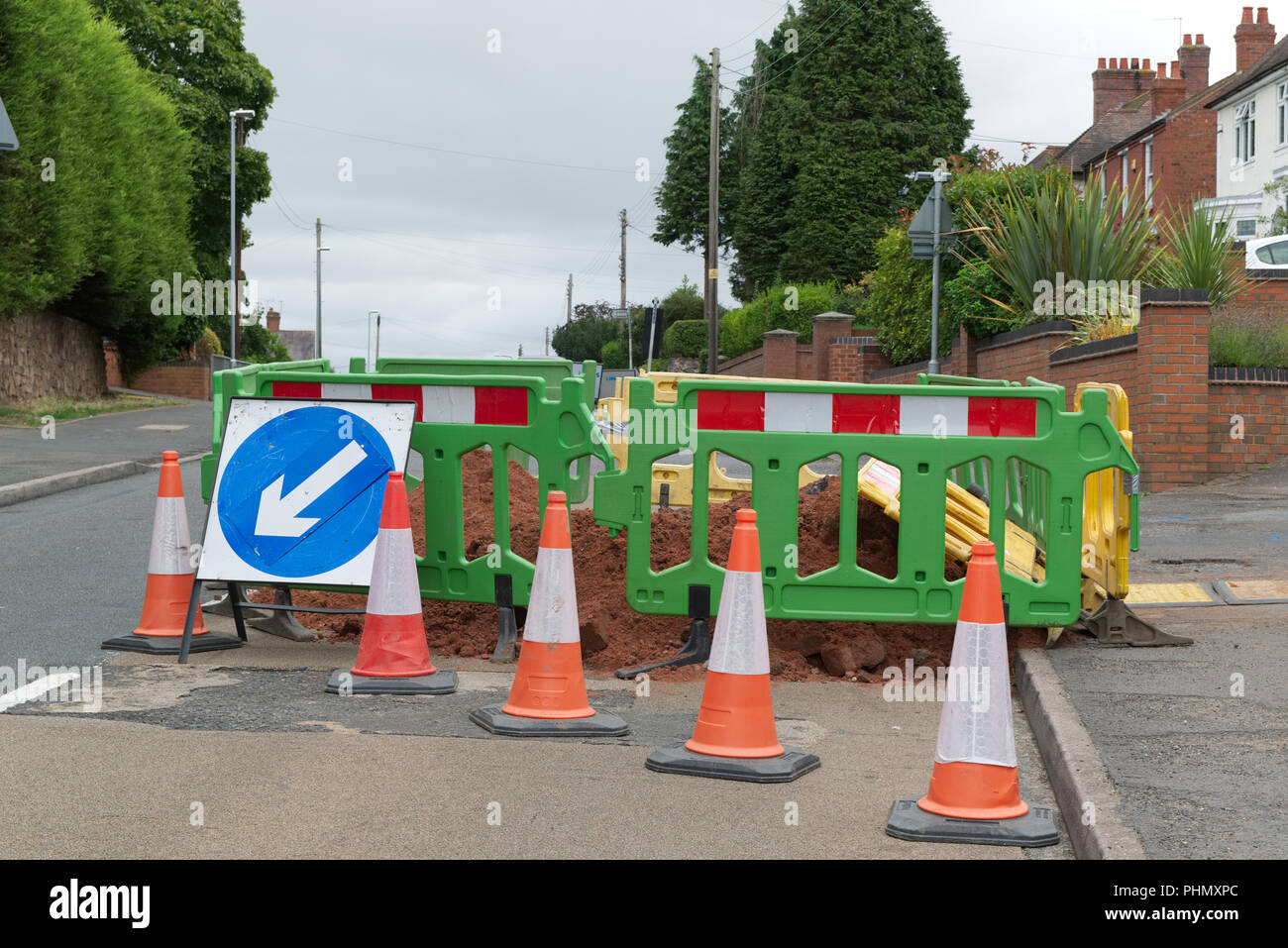 Roadworks in Kinver, Staffordshire, UK, with fenced off area around a hole in the road with yellow and green fence, road cones and signs Stock Photo
