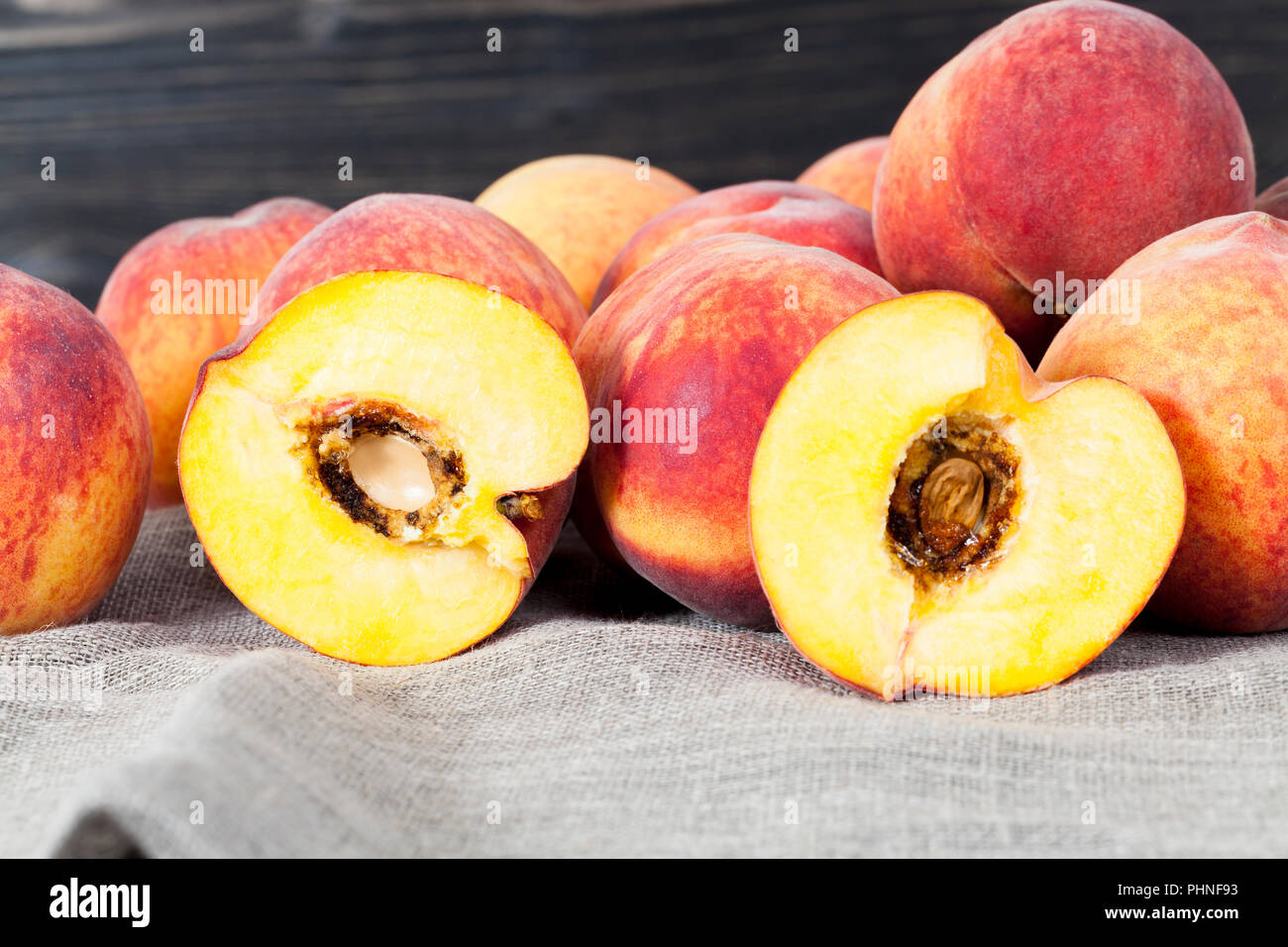 a bunch of peaches of orange color, one peach is cut into two halves and there is a bone in it with traces of putrefaction, although there is no outsi Stock Photo