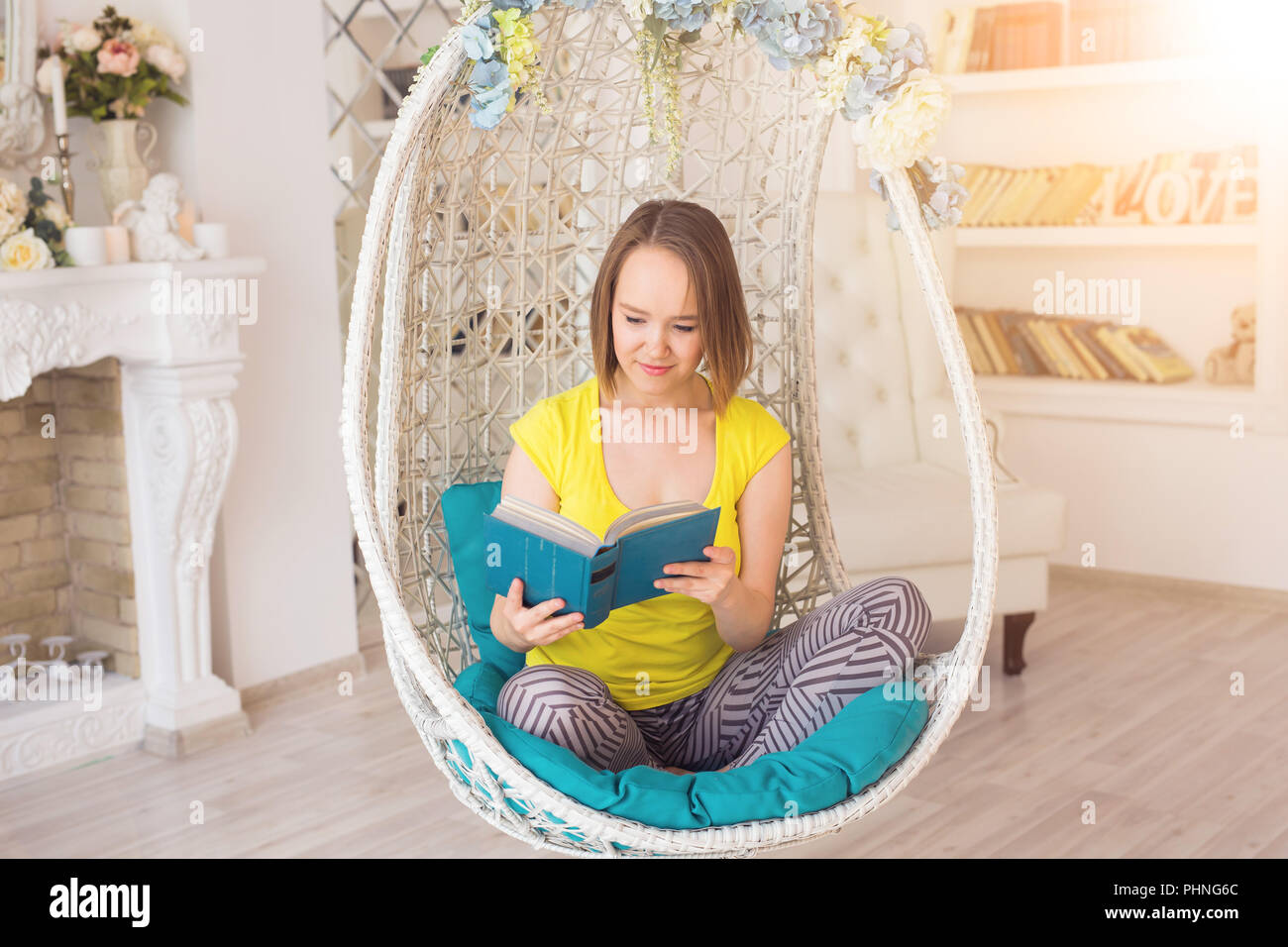 Young woman at home sitting on modern chair reading book Stock Photo ...
