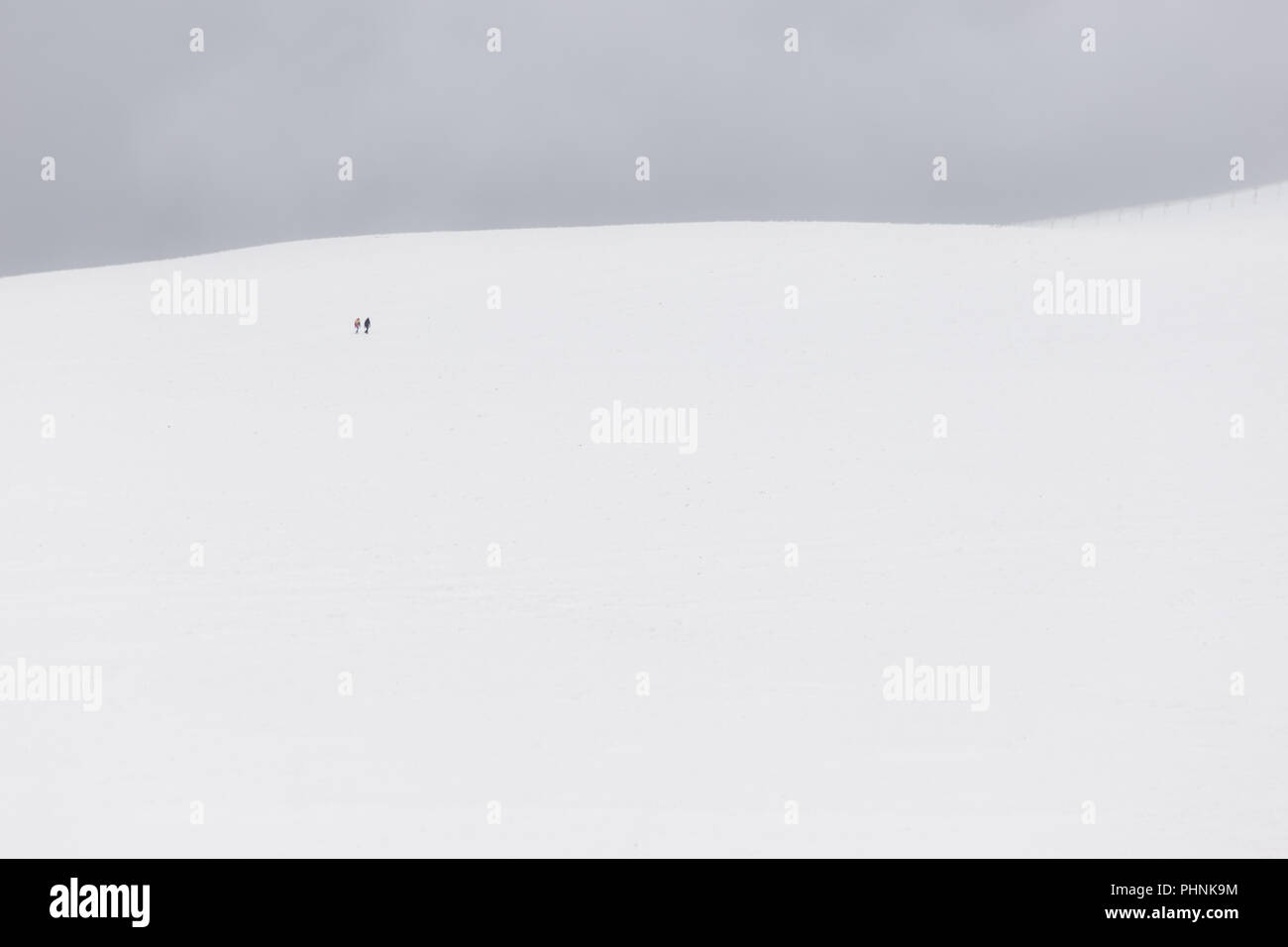 A very minimalistic view of two distant people over a mountain covered by snow Stock Photo