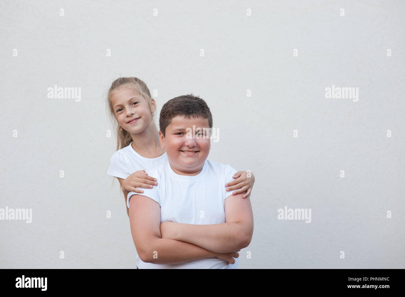 beautiful happy smiling kids thin caucasian girl in white shirt hugging fat boy copyspace Stock Photo
