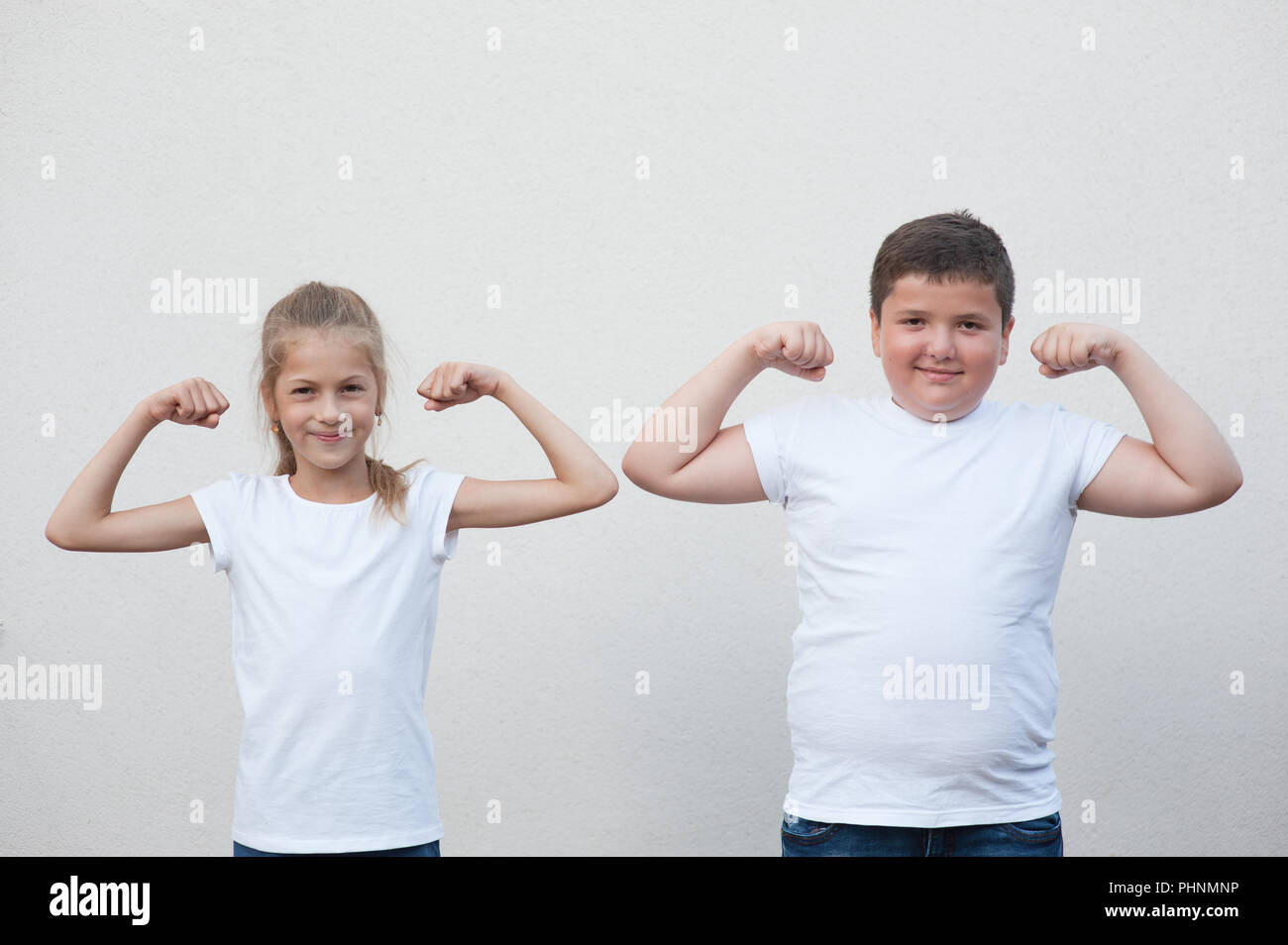 two children little thin girl and thick boy showing their muscle on copyspace background Stock Photo