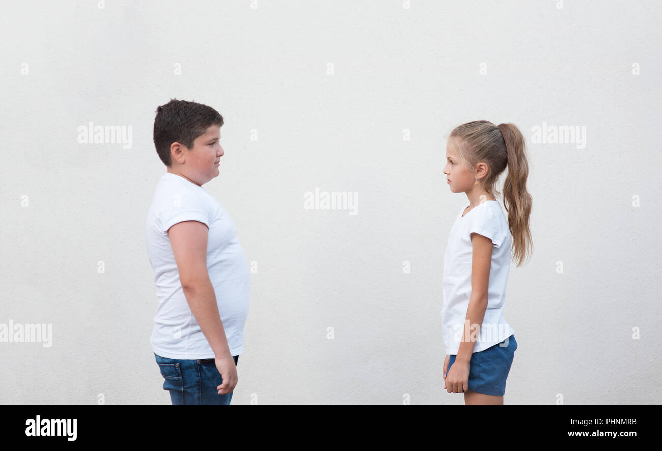 cute little thin girl and thick caucasian boy looking each other on copyspace background Stock Photo