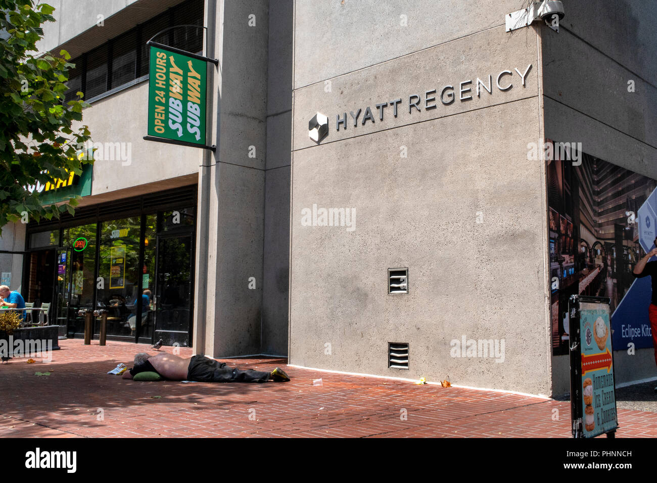 A homeless man sleeps on the street outside the Hyatt Regency hotel and a Subway in San Francisco, California. Stock Photo