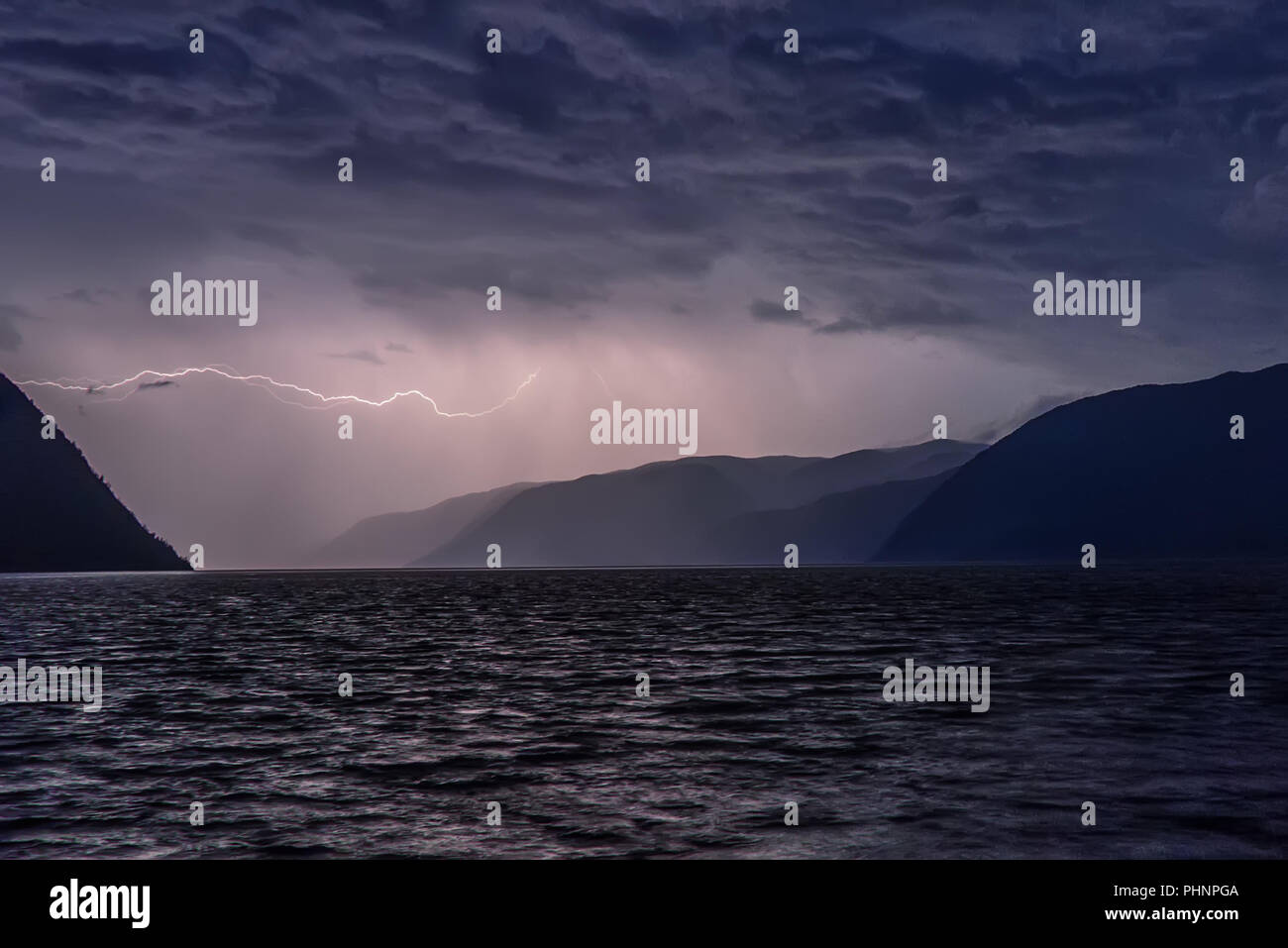 Amazing view with a flash of lightning in dark blue clouds during a thunderstorm over a lake in the mountains Stock Photo