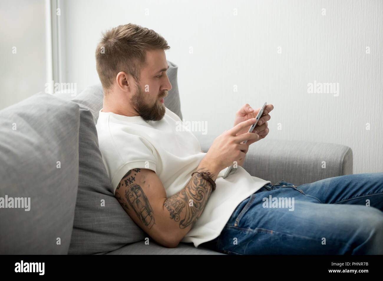 Millennial man sitting on couch holding tablet browsing web Stock Photo