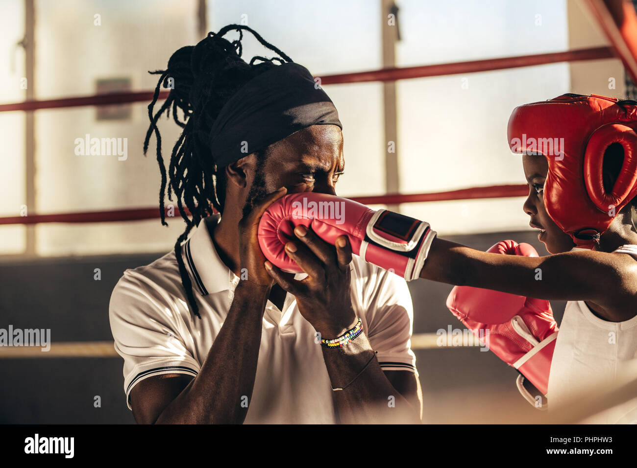 Kids wearing boxing gloves and headgear learning boxing from his coach