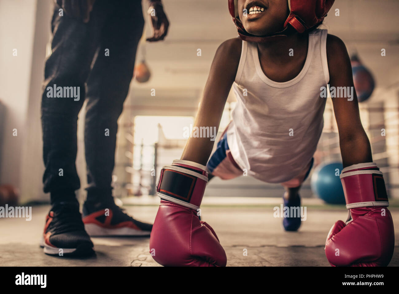 Boxing kid doing push ups wearing boxing gloves with his trainer