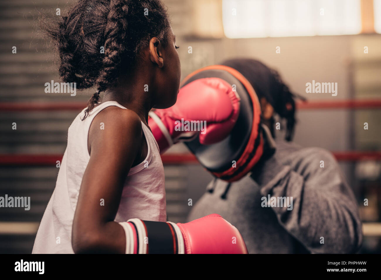 Girl wearing boxing gloves straining with her coach. Boxing kid