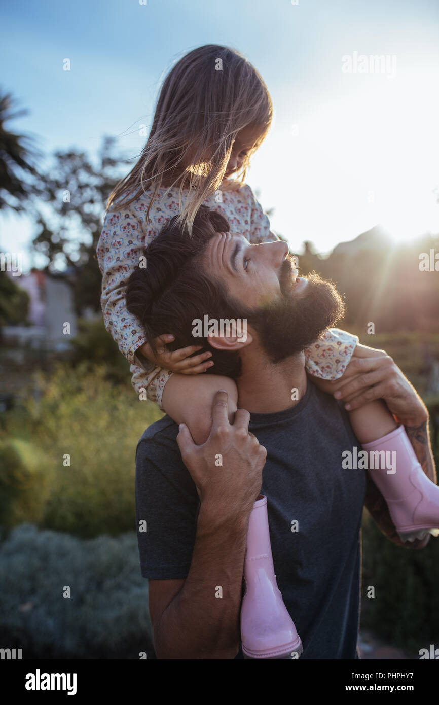 Portrait of a father carrying his daughter on shoulders at field. Little girl riding on father's shoulders. Stock Photo