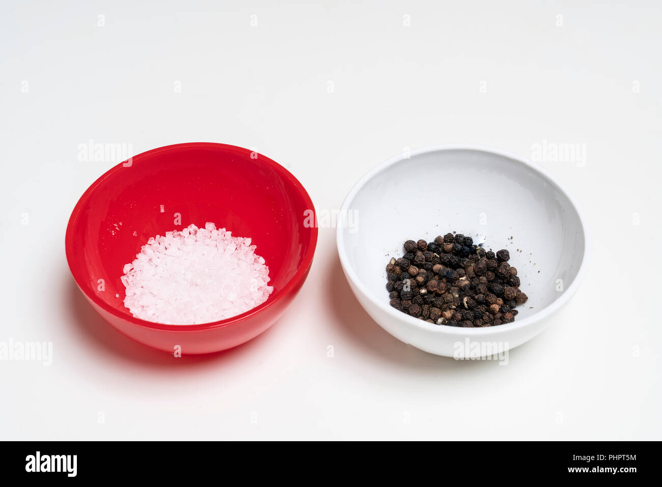 two colored bowls containing coarse salt and peppercorns Stock Photo