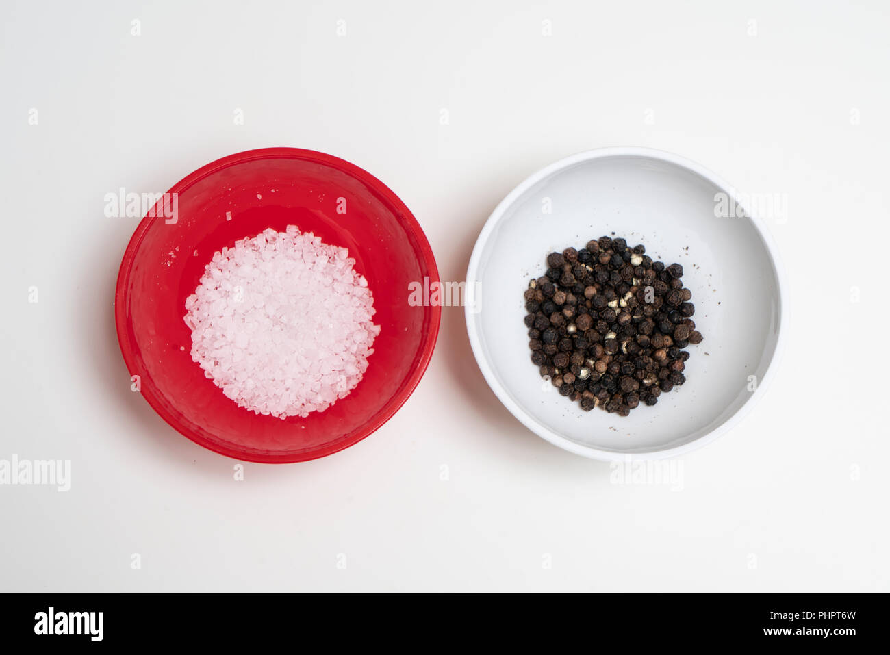 two colored bowls containing coarse salt and peppercorns Stock Photo