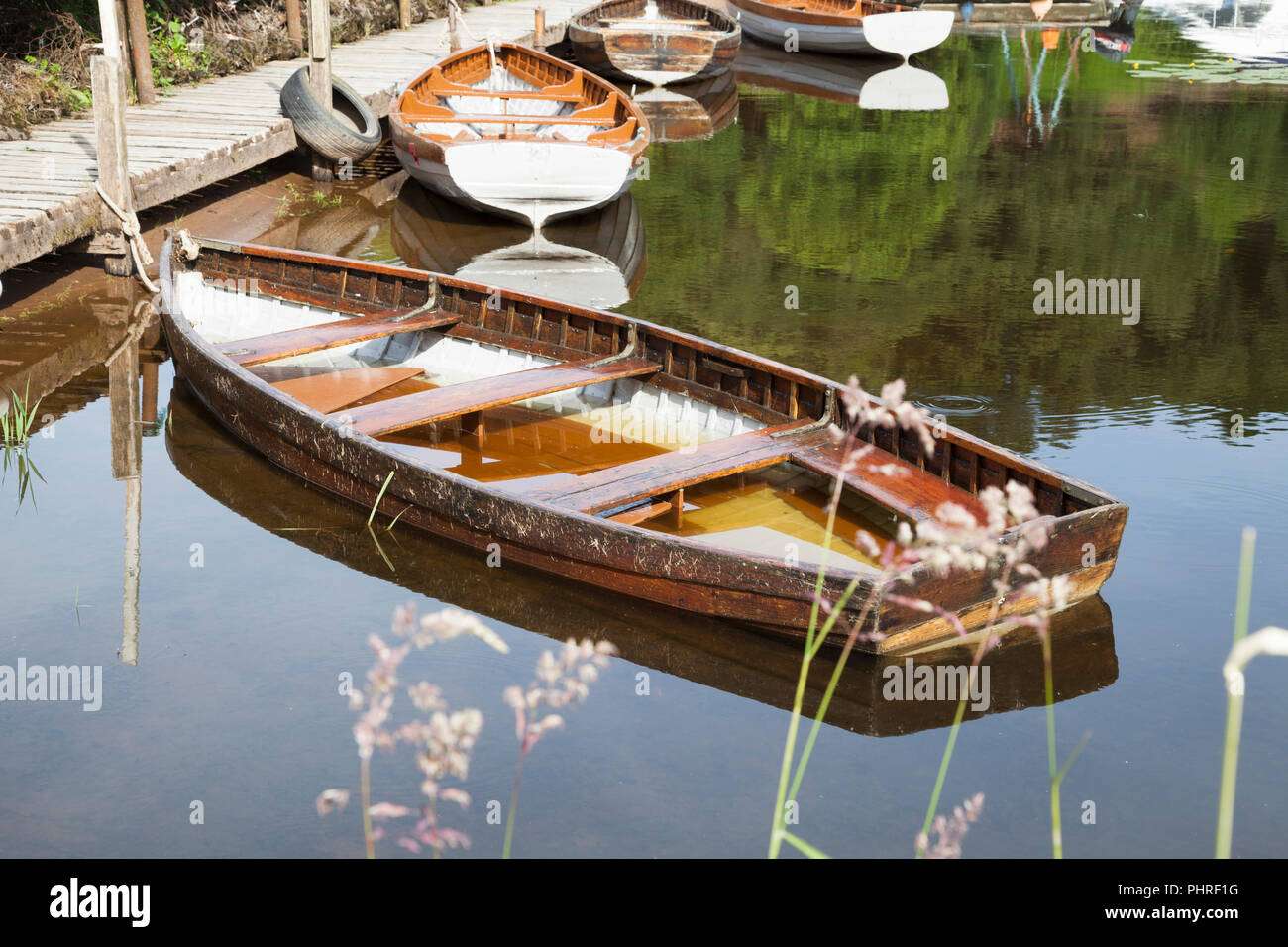 Waterlogged rowing boat at Balmaha, Loch Lomond Scotland, tied to jetty with reflections. Stock Photo