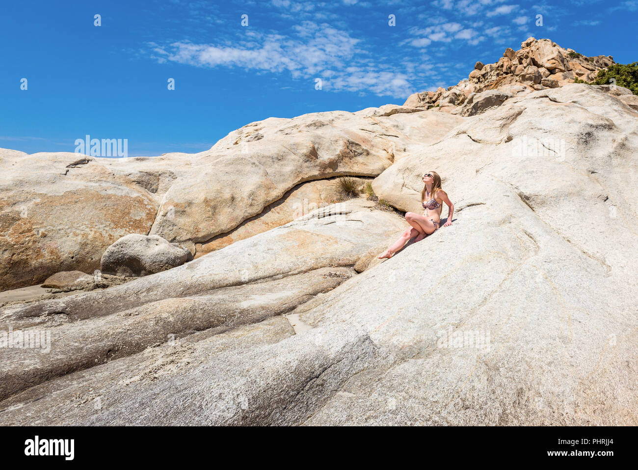 A beautiful young woman sitting on a rock in summer day. Naxos, Greece Stock Photo