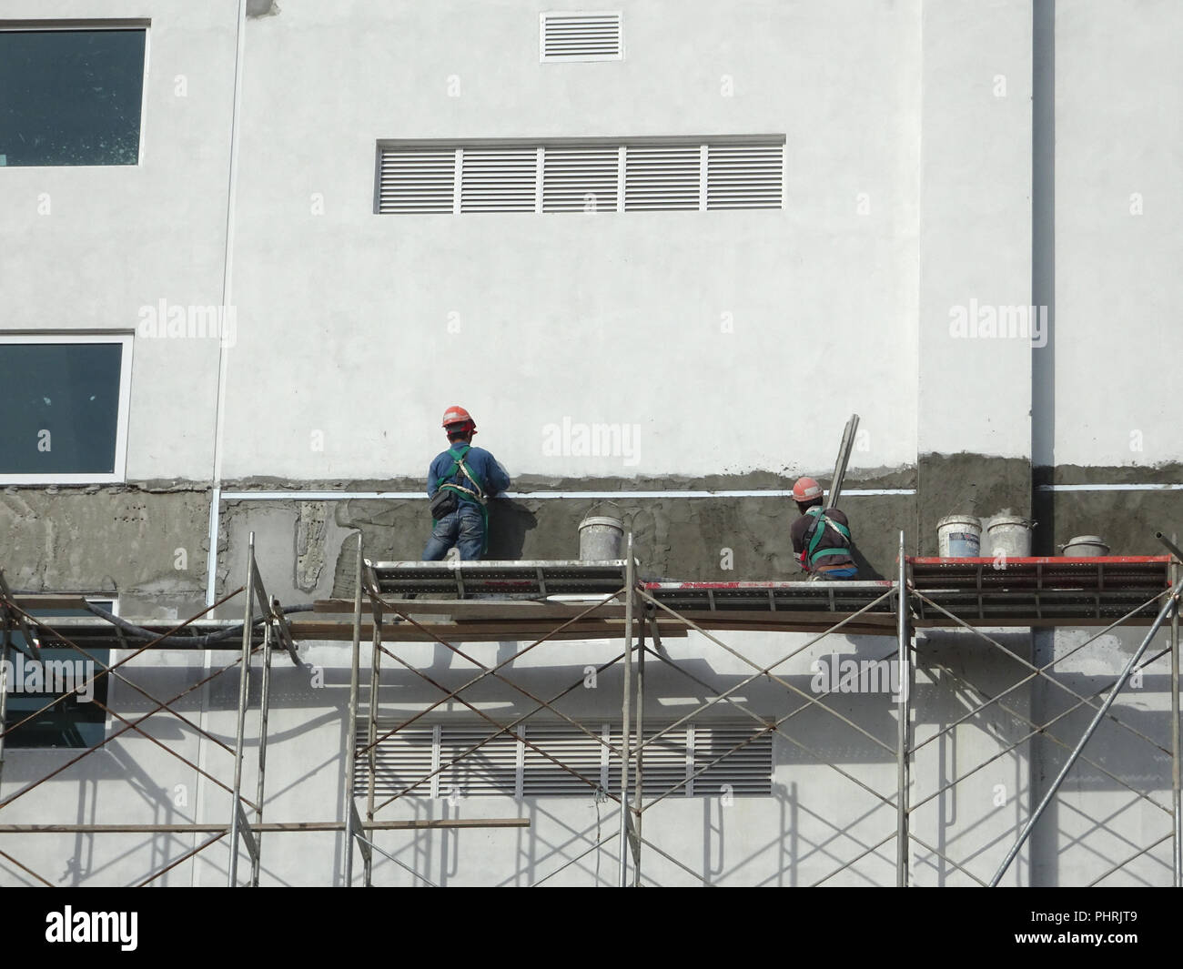 Construction workers plastering wall using cement plaster at the construction site. They are wearing appropriate safety gear to prevent bad happen Stock Photo