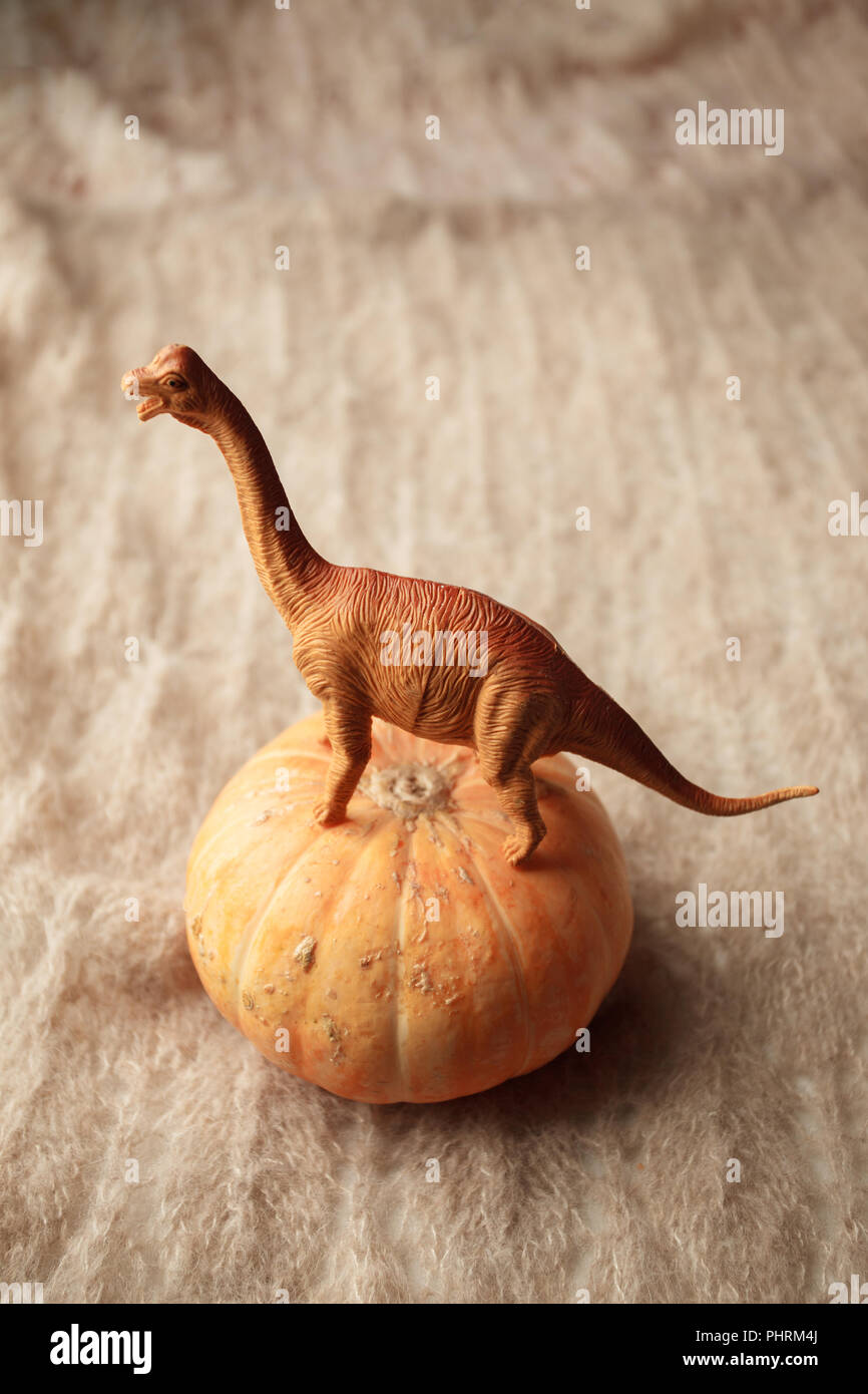 A dinosaur stands on a pumpkin on a brown background, a surreal concept, a monochrome Stock Photo