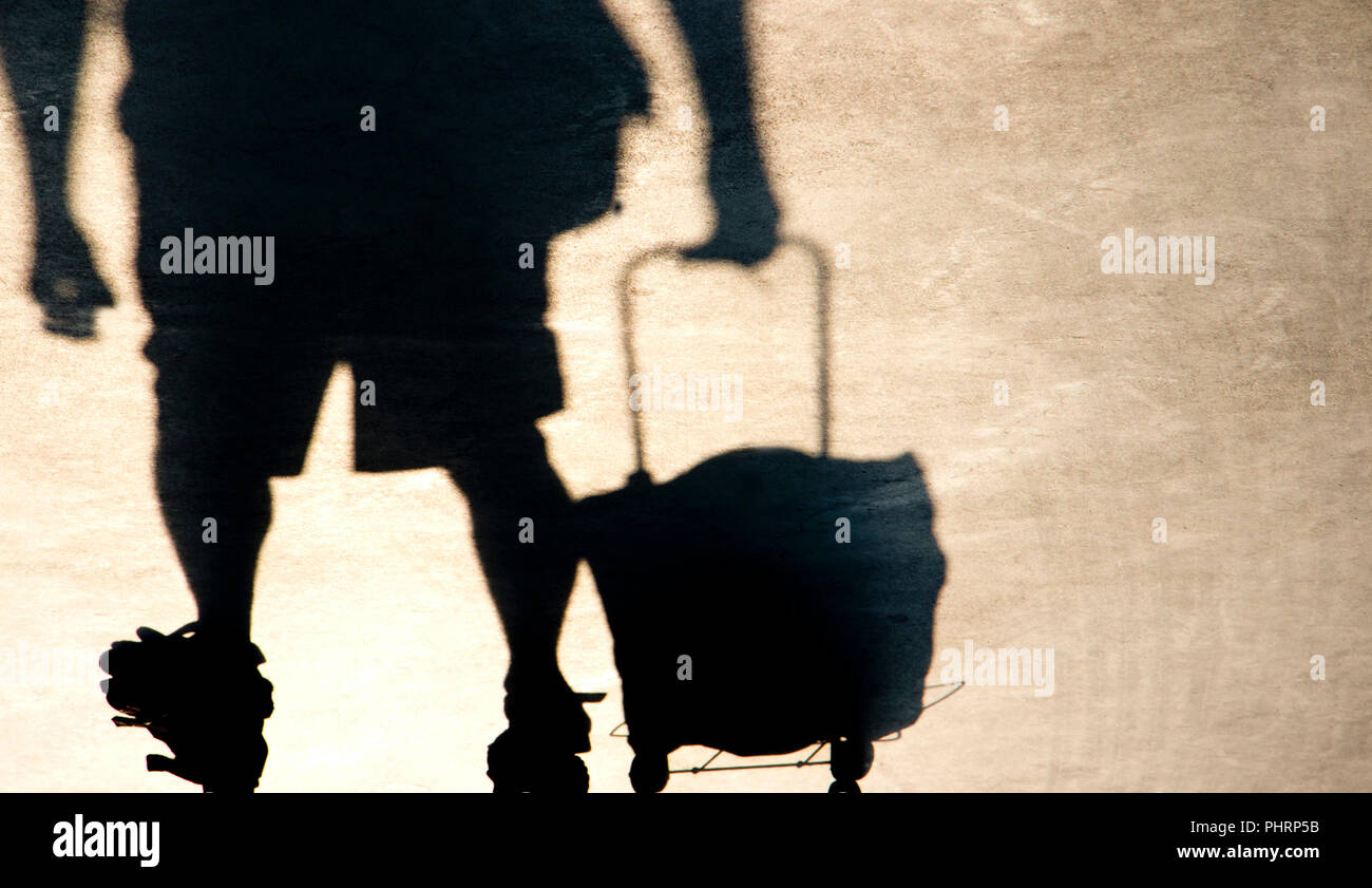 Shadow silhouette of elderly man pulling a shopping trolley grocery bag , from waist down in sepia black and white Stock Photo
