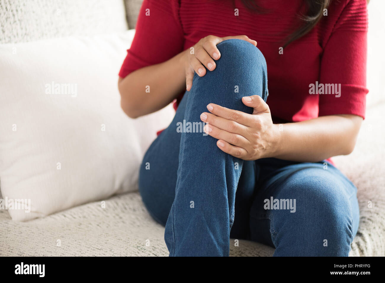 Closeup young woman sitting on sofa and feeling knee pain and she