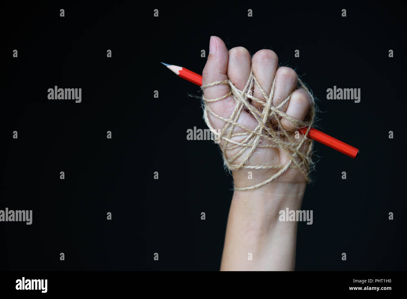 Hand with red pencil tied with rope, depicting the idea of freedom of ...